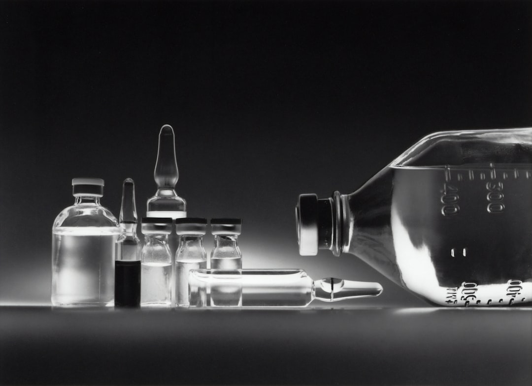 Glass medical vials and a large intravenous fluid bottle on a dark surface