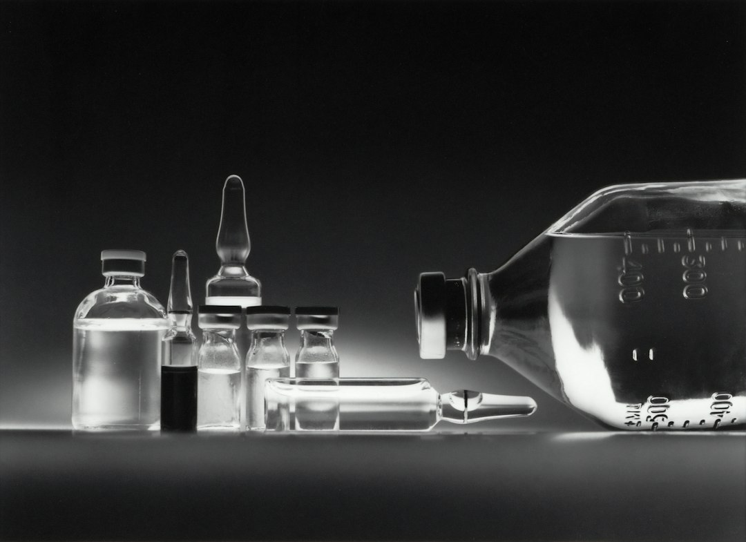 Glass medical vials and a large intravenous fluid bottle on a dark surface